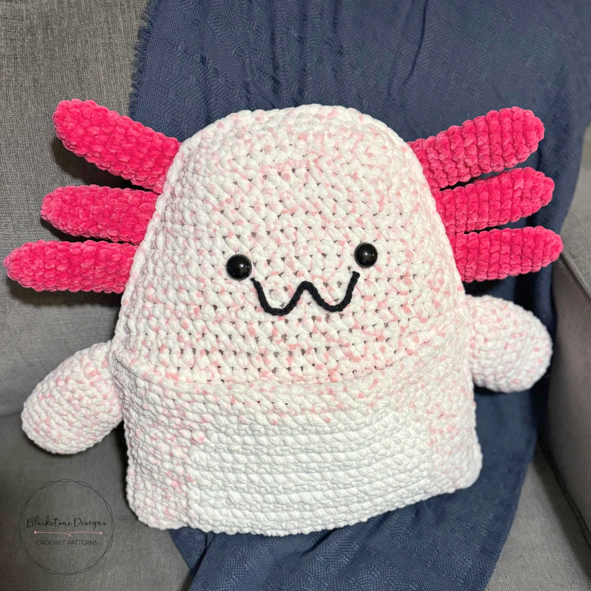 Crochet Axolotl Pillow with Book Pocket belly, made with light pink yarn for the body and dark pink for the external gills
