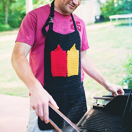 BBQ Toolbelt Apron Crochet Pattern. Man wearing Black crochet apron in front of a grill.